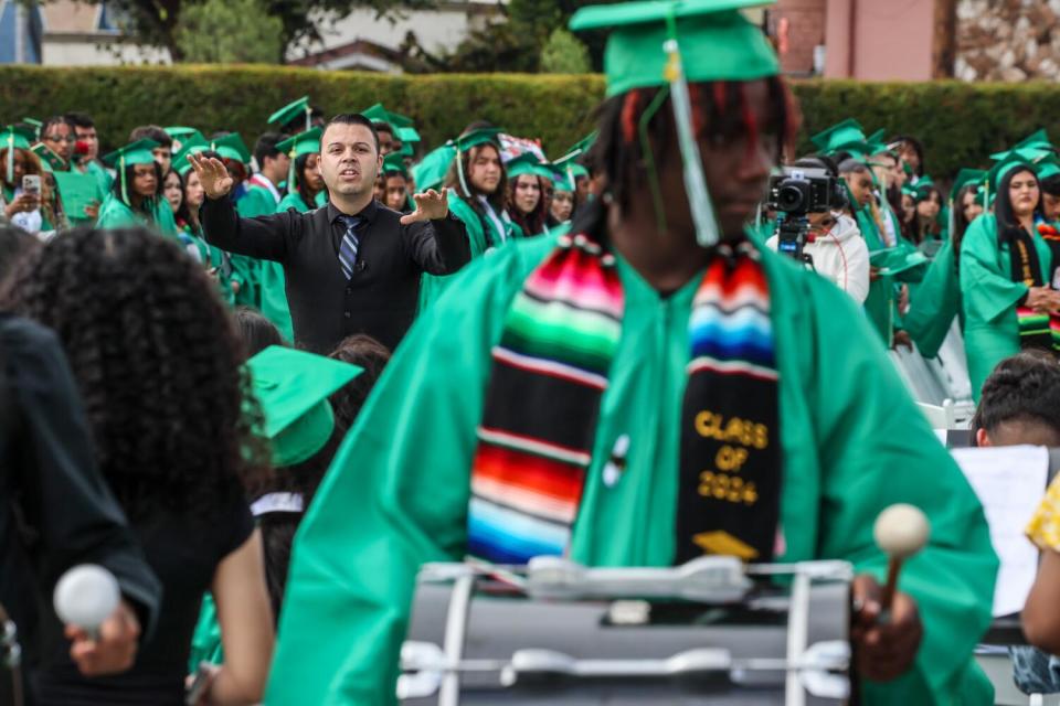 Marching band members in green robes play outdoors.