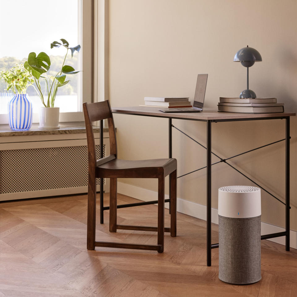 A cylindrical air purifer by a desk in a home office