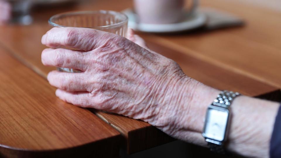 An elderly person holds a cup