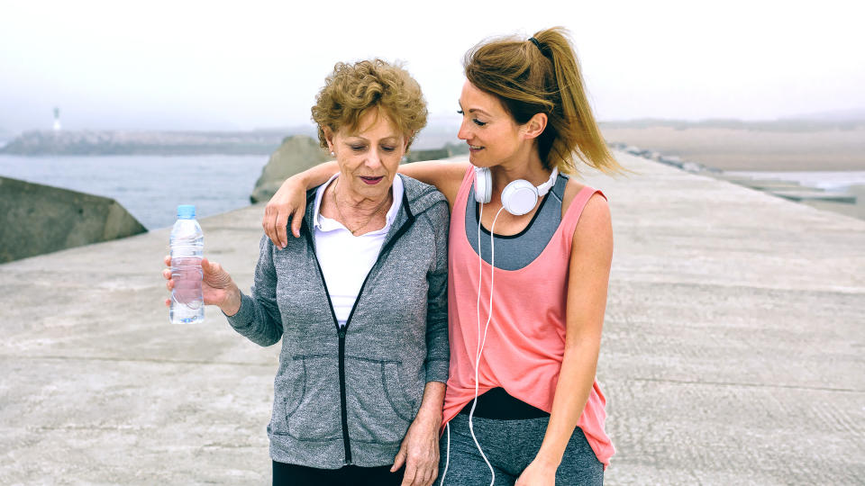 Senior woman and young woman walking outdoors by sea pier.