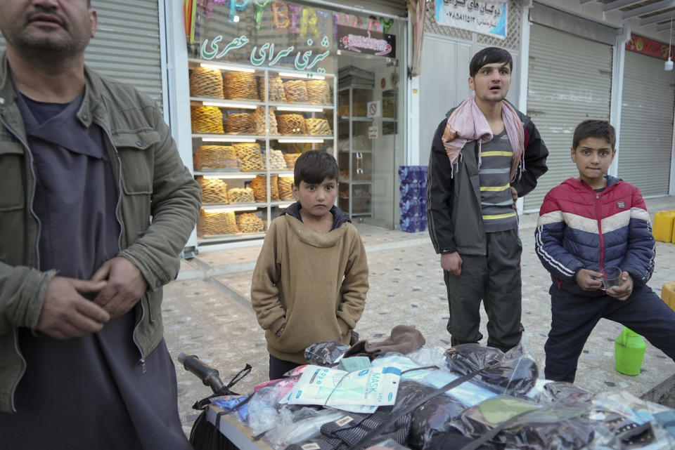 Sanam -- a bacha posh, a girl living as a boy, stands next to her father at their street stand selling masks, in Kabul, Afghanistan, Tuesday, Dec. 7, 2021. In the heavily patriarchal, male-dominated society of Afghanistan, where women and girls are usually relegated to the home, there is one tradition which allows girls access to the male world: bacha posh. A girl dresses, behaves and is treated as a boy, allowing her to play and to work as a boy would be able to do, until she reaches puberty. (AP Photo/Mstyslav Chernov)