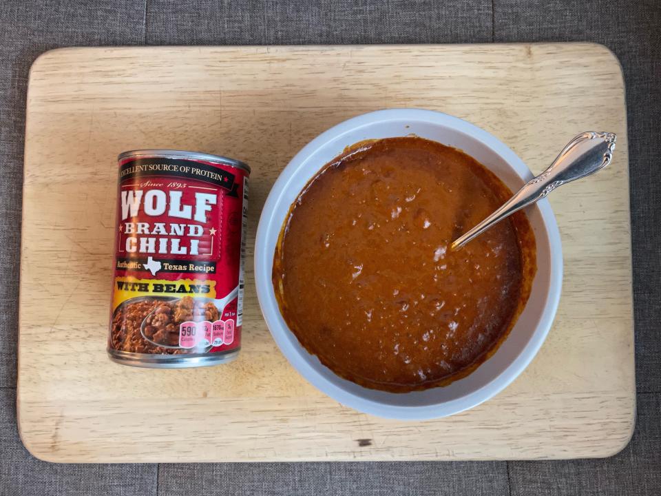 Red can of wolf brand chili beside white bowl of it