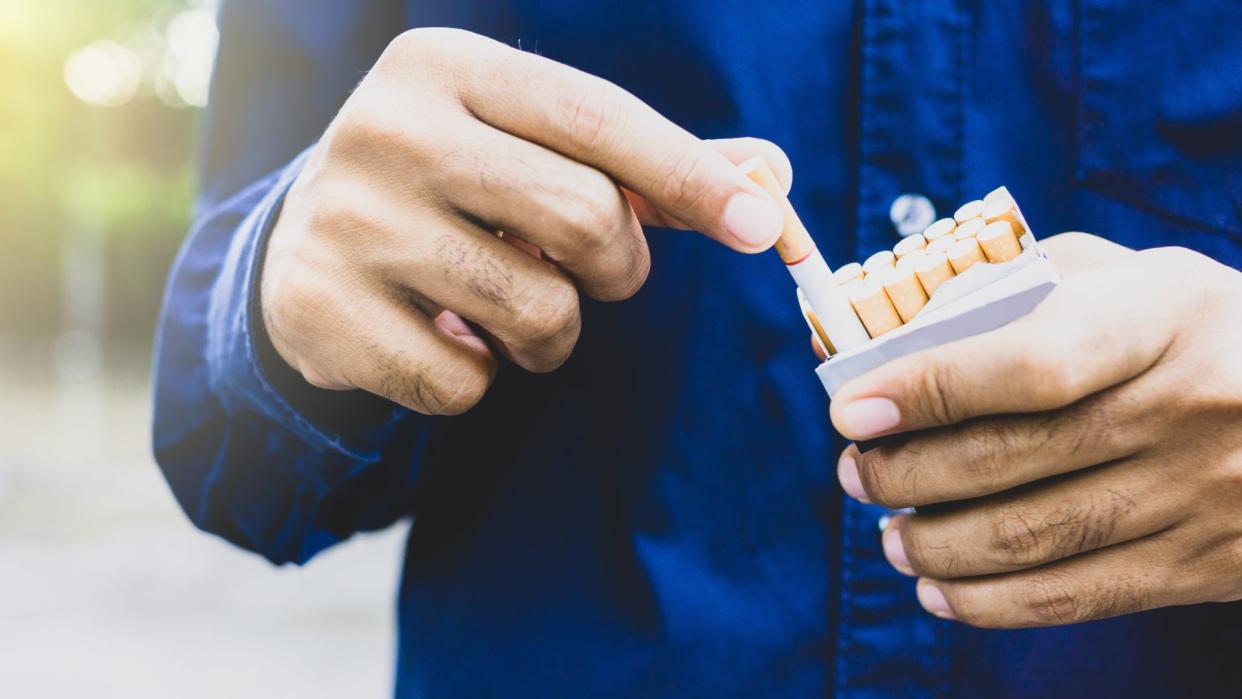  photo shows a man's hands as he pulls a cigarette from a full pack 