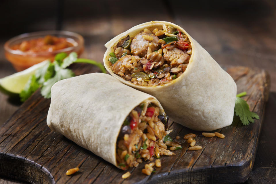 A burrito with rice and beans falling out on a cutting board