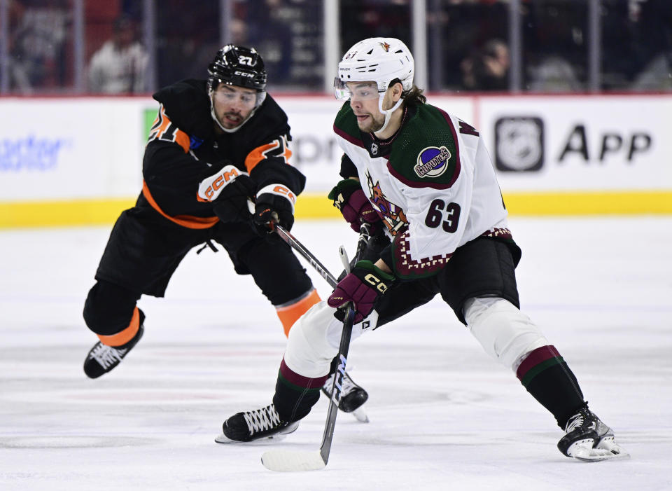 Arizona Coyotes' Matias Maccelli (63) skates with the puck past Philadelphia Flyers' Noah Cates, left, during the first period of an NHL hockey game, Monday, Feb. 12, 2024, in Philadelphia. (AP Photo/Derik Hamilton)