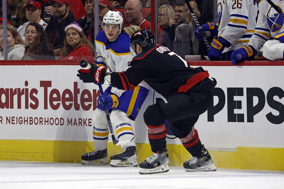 Buffalo Sabres' Zach Benson (9) flips the puck past Carolina Hurricanes' Dmitry Orlov (7) during the first period of an NHL hockey game in Raleigh, N.C., Saturday, Dec. 2, 2023. (AP Photo/Karl B DeBlaker)