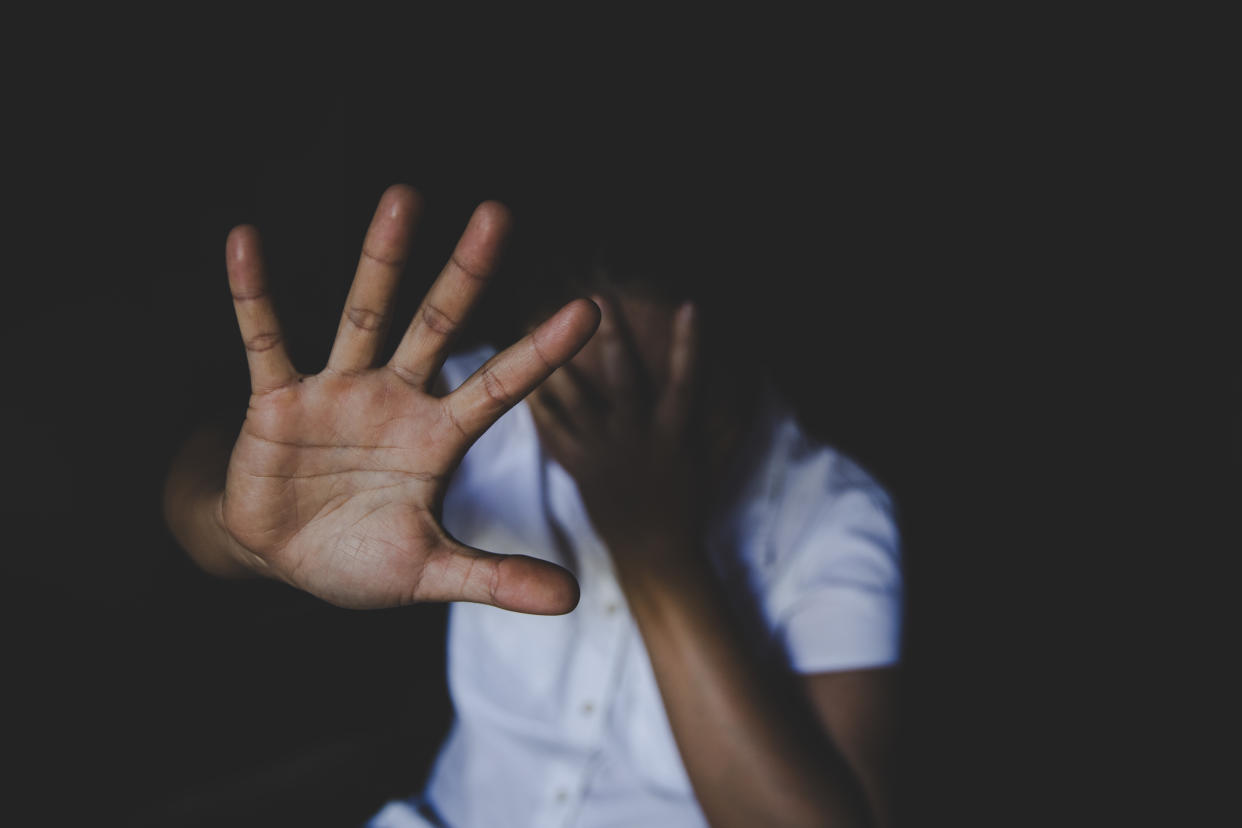 A woman with her face covered and hand raised.