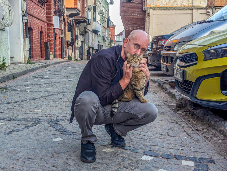 Brent crouched down holding a cat on his knee that he's petting