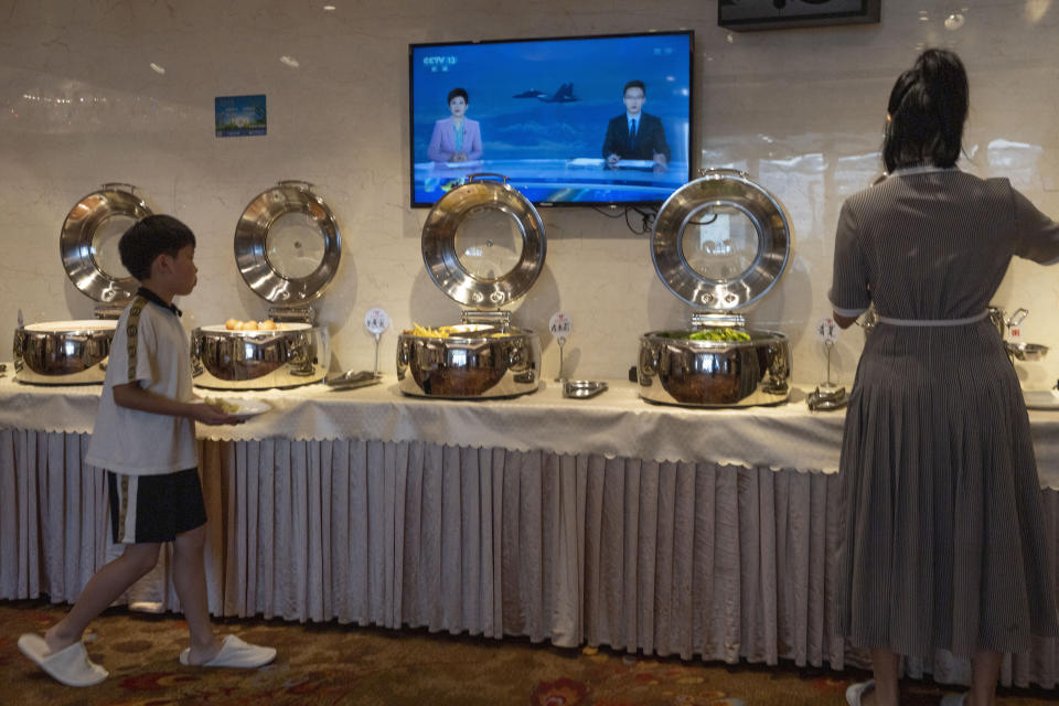 Hotel guests collect food from a breakfast buffet as a news broadcast report on the military exercises, in Pingtan in eastern China's Fujian province, Saturday, Aug. 6, 2022. China cut off contacts with the United States on vital issues Friday — including military matters and crucial climate cooperation — as concerns rose that the Communist government's hostile reaction to House Speaker Nancy Pelosi's Taiwan visit could signal a lasting, more aggressive approach toward its U.S. rival and the self-ruled island. (AP Photo/Ng Han Guan)