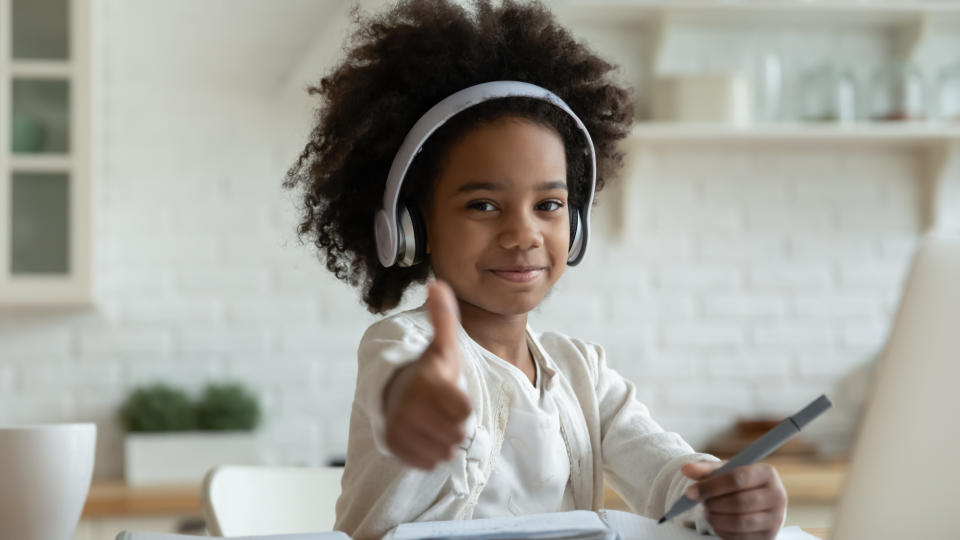 Kid wearing large headphones while writing in a notebook giving thumbs up