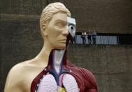 Visitors stand at a balcony behind the Damien Hirst sculpture "Hymn" outside the Tate Modern gallery in London August 21, 2012.