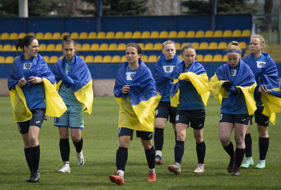 Players of a women's football team from Mariupol draped in Ukrainian national flags go in a stadium before a Ukrainian championship match against Shakhtar in Kyiv, Ukraine, Tuesday, April 18, 2023. After their city was devastated and captured by Russian forces, the team from Mariupol rose from the ashes when they gathered a new team in Kyiv. They continue to play to remind everyone that despite the occupation that will soon hit one year, Mariupol remains a Ukrainian city. (AP Photo/Efrem Lukatsky)
