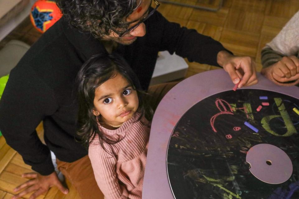 A child looks up as her father points to an arts project on a table.