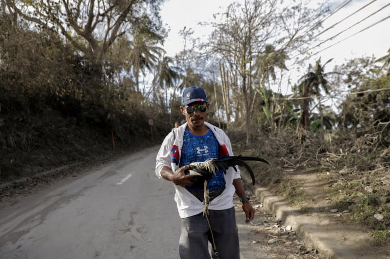 A man carrying a chicken flees from his town following Taal Volcano's eruption, in Talisay, Batangas