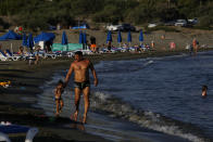 A father with his child walks along Saint Rafael beach in southern coastal city of Limassol, Cyprus, on Wednesday, July 29, 2020. Cyprus' Tourism Minister Savvas Perdios says the country doesn't expect to receive this year more than 20-25% of the record 3.97 million holidaymakers it welcomed in 2019 as the coronavirus pandemic has so far shut out its key tourism markets. (AP Photo/Petros Karadjias)