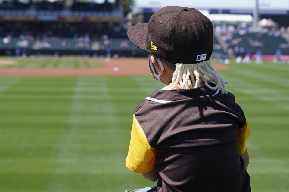 Five-year-old Geronimo Morales wears a hat with fake dreadlocks to mimic San Diego Padres' Fernando Tatis Jr., as he sits on the shoulders of his father, Richard Morales, as they watch the Padres warm up before a spring training baseball game against the Kansas City Royals, Monday, March 22, 2021, in Surprise, Ariz. (AP Photo/Sue Ogrocki)
