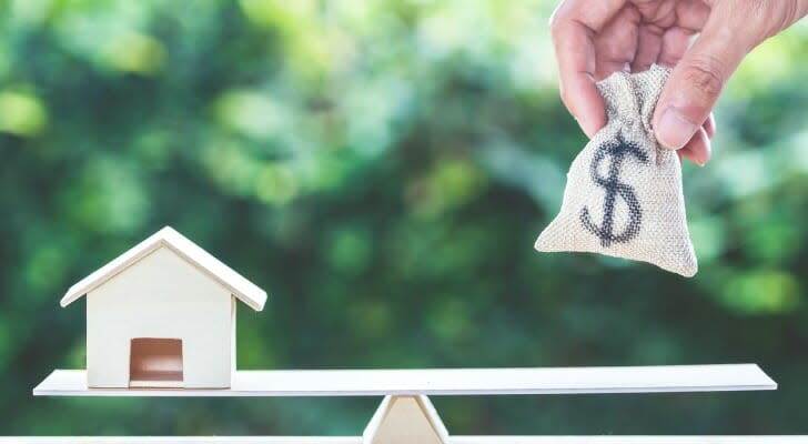 Model house and bag of cash on opposite ends of a see-saw