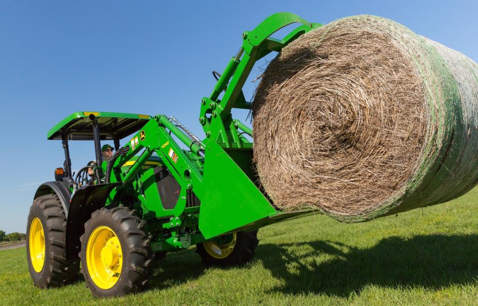 Green tractor holding a bale of hay.