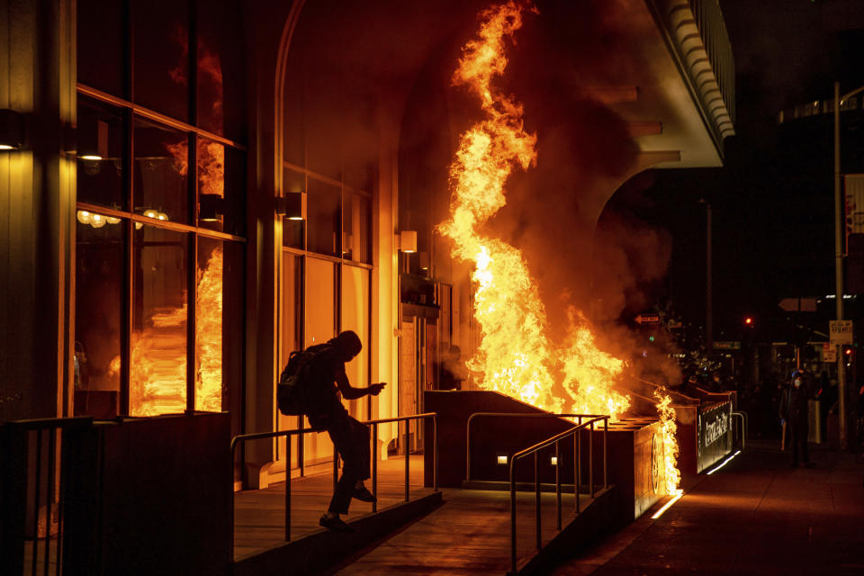 Manifestantes prenden fuego al frente del edificio de California Bank y Trust durante una protesta contra la brutalidad policial en Oakland, California, la noche del viernes 16 de abril de 2021. (AP Foto/Ethan Swope)