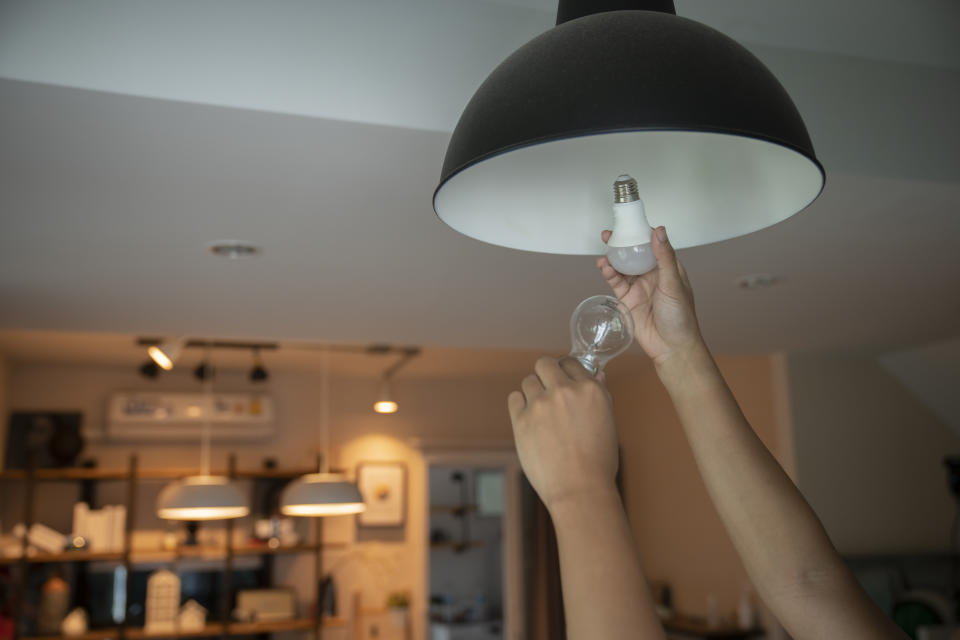 With two comparable light fixtures on in the background, someone holds a compact-fluorescent bulb in their right hand and a new LED bulb in their left hand. (Getty images)