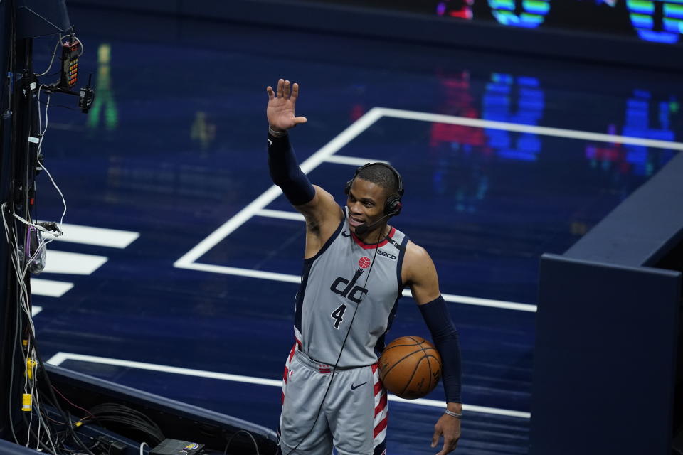Russell Westbrook holds a game ball and waves with his other hand while wearing a headset during a postgame interview.