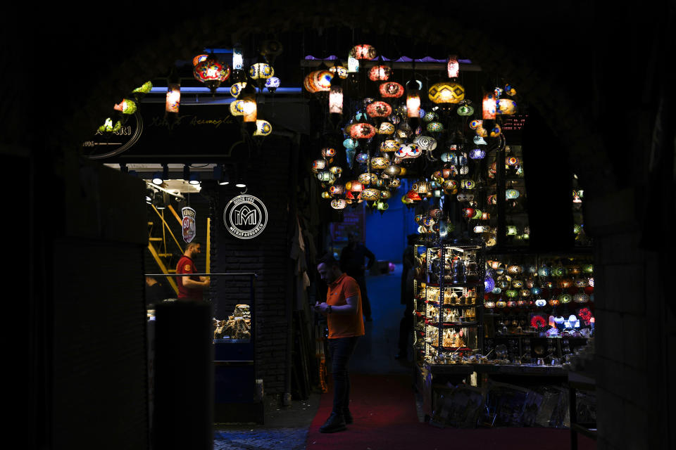 A man stands next to decorative lights hanging outside a shop at an outdoor market in Istanbul, Turkey, Tuesday, June 20, 2023. The Turkish central bank faces a key test Thursday June 22, 2023, on turning to more conventional economic policies to counter sky-high inflation after newly reelected President Recep Tayyip Erdogan gave mixed signals about an approach that many blame for worsening a cost-of-living crisis. (AP Photo/Khalil Hamra)