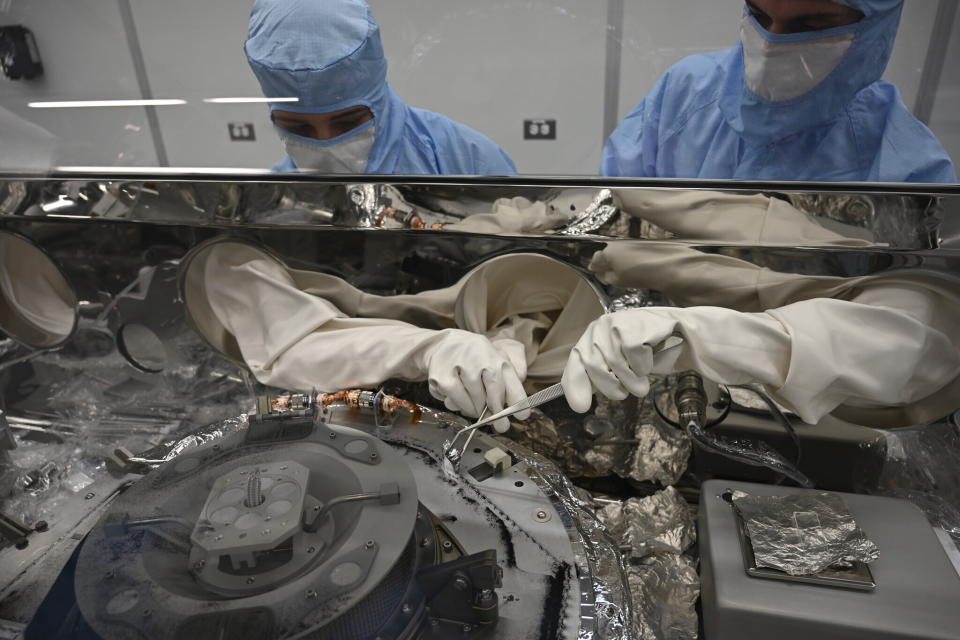 In this photo provided by NASA, Mari Montoya, left, and Curtis Calva, right, use tools to collect asteroid particles from the base of a canister on Sept. 27, 2023, at Johnson Space Center in Houston. NASA on Wednesday, Oct. 11, 2023, showed off its first asteroid samples delivered last month by the Osiris-Rex spacecraft, a jumble of black dust and rubble that's the most ever returned to Earth. (NASA via AP)