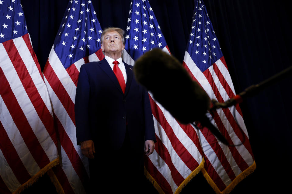 Donald Trump stands tall in front of four American flags.