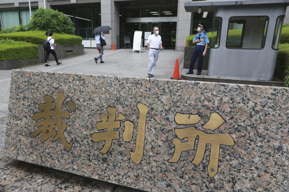 People walk in the compound of the Tokyo District Court where a trial of two Americans suspected of helping former Nissan chairman Carlos Ghosn flee Japan, opens in Tokyo, Monday, June 14, 2021. The court is starting the trial of trial of Michael Taylor, a former Green Beret, and his son Peter Taylor in connection with the brash escape of Ghosn from Japan to Lebanon in late 2019. The Japanese plate reads: "Court." (AP Photo/Koji Sasahara)