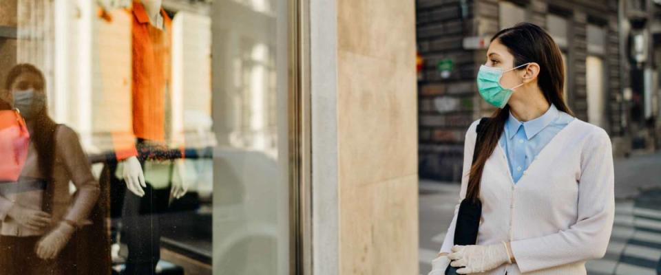 Woman with mask looking at a closed fashion clothes storefront.