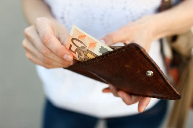 Girl is taking out a banknote of fifty euros from brown leather wallet on the street. Hands, money and wallet close-up