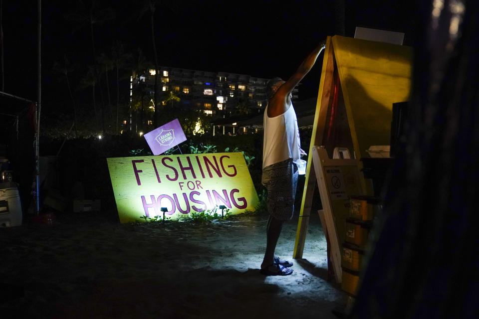 Naldo Valentine, who lost his home to the Lahaina wildfire, puts up a light as darkness falls at a housing protest on Kaanapali Beach Wednesday, Dec. 6, 2023, in Lahaina, Hawaii. A group of survivors is camping on the resort beach to protest and raise awareness for better long-term housing options for those displaced. Residents and survivors still dealing with the aftermath of the August wildfires in Lahaina have mixed feelings as tourists begin to return to the west side of Maui, staying in hotels still housing some displaced residents. (AP Photo/Lindsey Wasson)