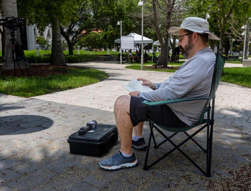 Orlando Montejo, a cameraman for WSVN, Channel 7, Miami, reads a book under the shade of a palm tree in front of the Federal courthouse in Miami as a grand jury gathers evidence related to the possible mishandling of classified documents by former President Donald J. Trump.