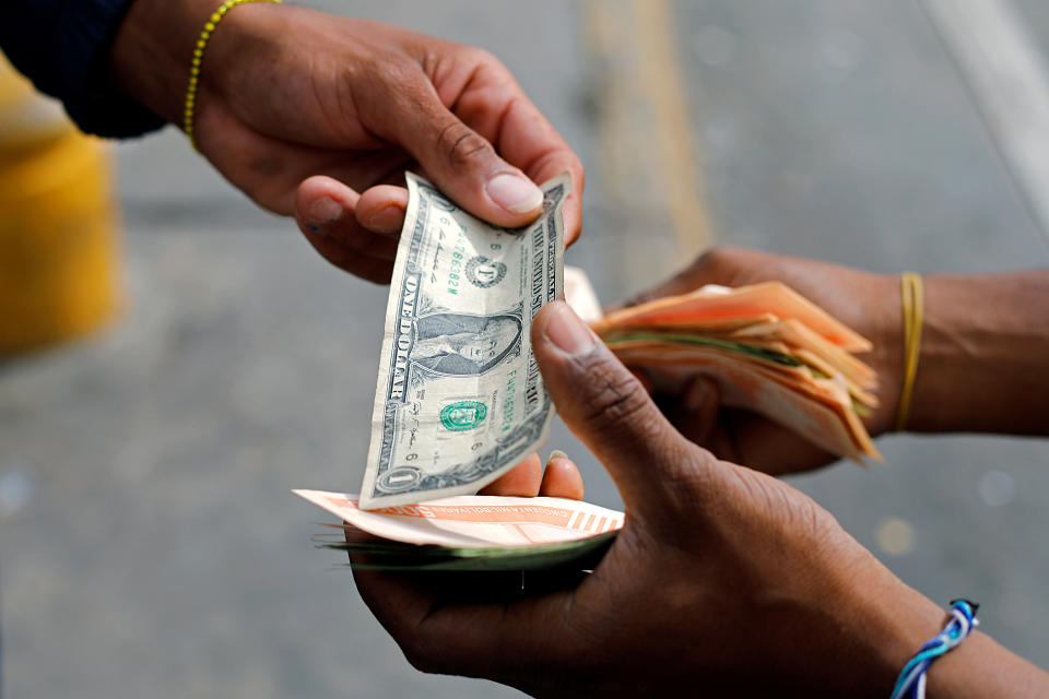 A man changes a dollar bill with the bus driver's assistant, who is holding a wad of Bolivar banknotes, at a bus stop outside the Antimano metro station in Caracas, Venezuela March 9, 2021. Picture taken March 9, 2021. REUTERS/Leonardo Fernandez Viloria