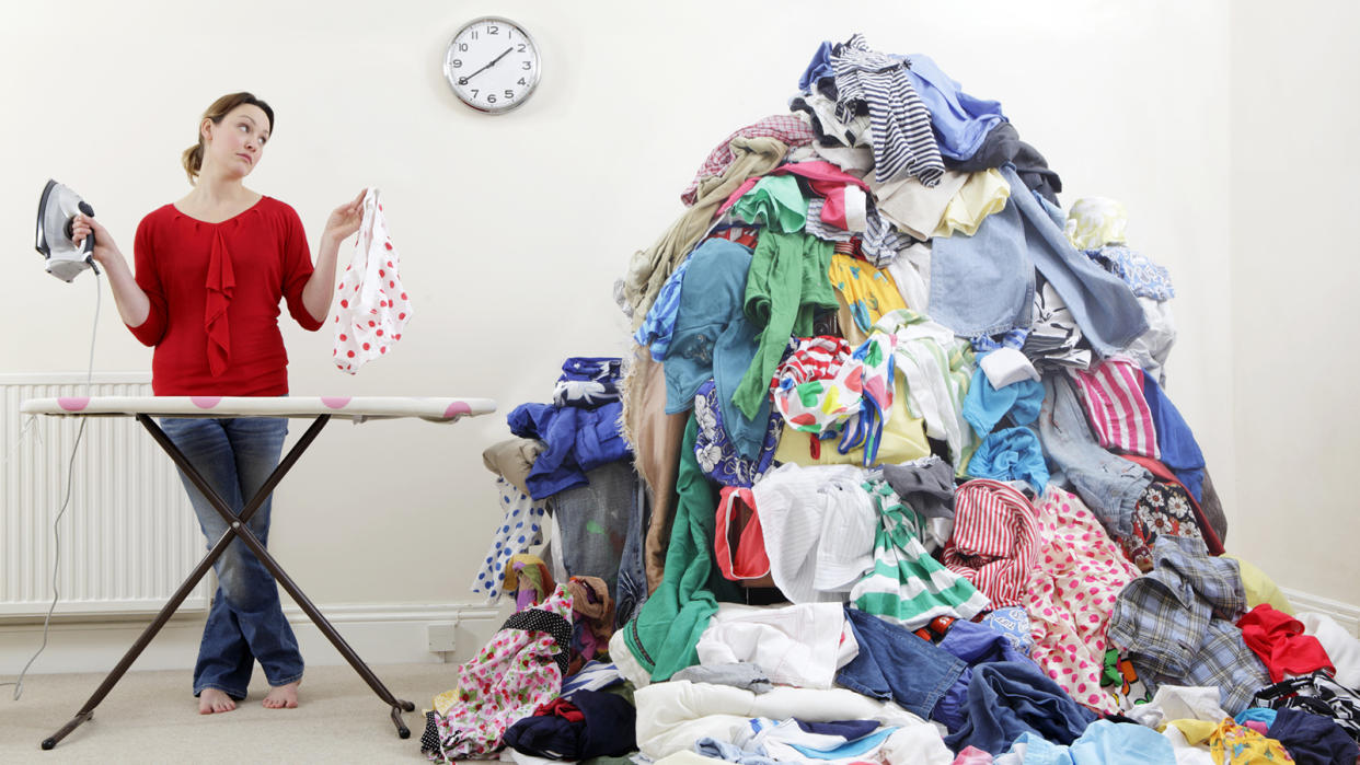 Woman with iron and ironing board standing beside giant pile of laundry