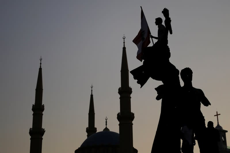 A demonstrator holds a Lebanese national flag as he sits atop a statue on Martyrs' square, as the Al-Amin mosque is seen in the background, during an anti-government protest in downtown Beirut