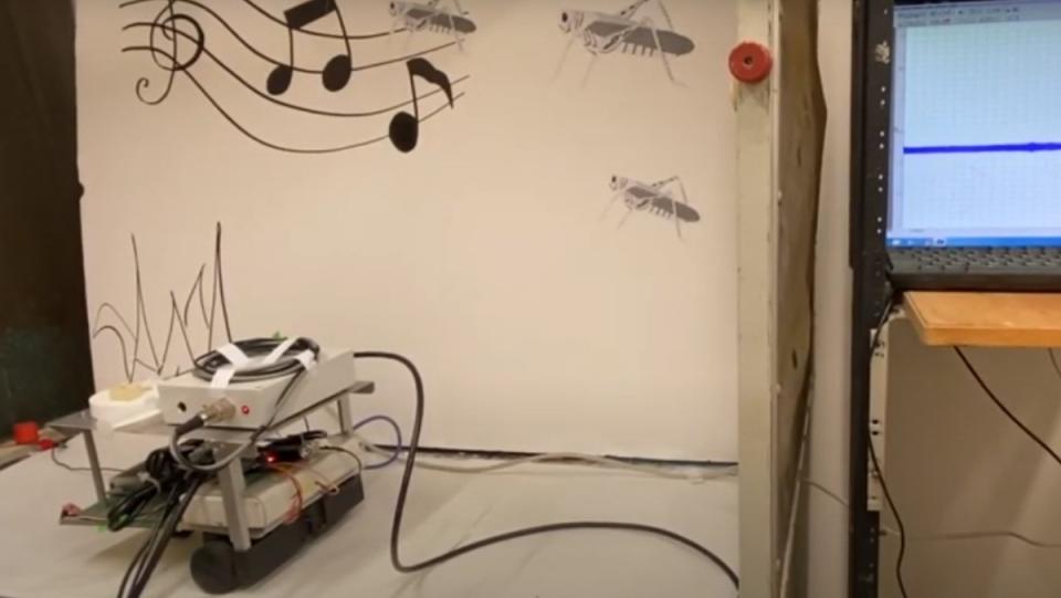 a photo of a small white robot called ear-bot on a table responding to hand claps from a nearby computer