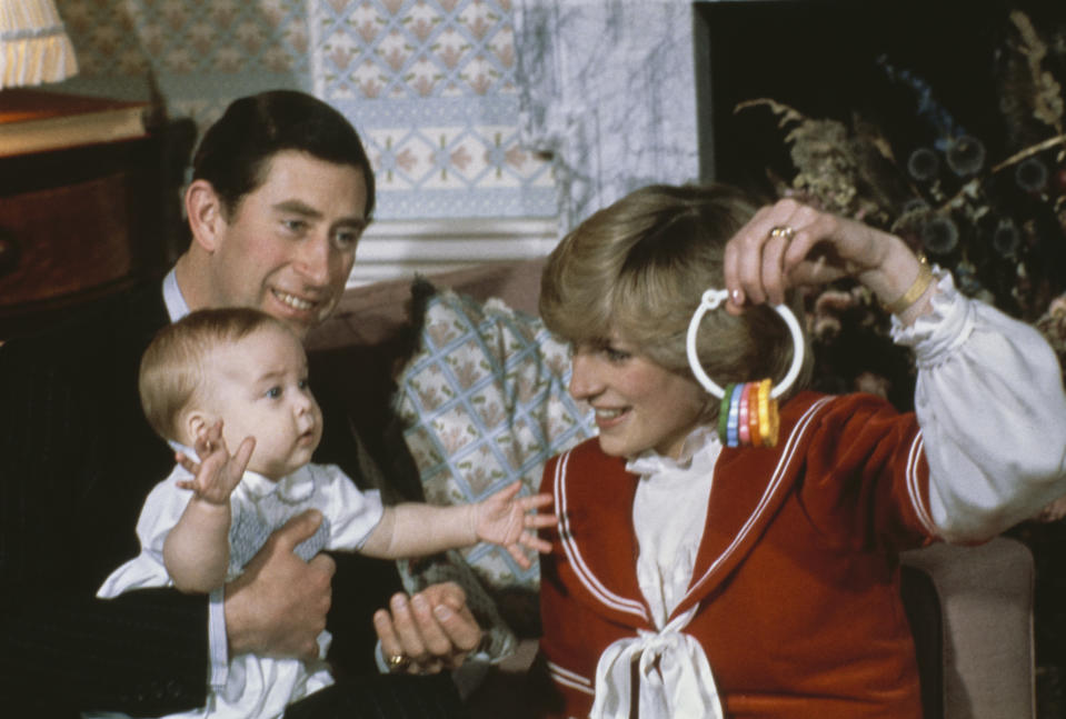 British Royals Charles, Prince of Wales holds his baby son, Prince William, with his wife, Diana, Princess of Wales, wearing a red-and-white bow-fronted outfit, who dangles a teething ring in front of her son, at their Kensington Palace home in London, England, 22nd December 1982. (Photo by Fox/Keystone/Hulton Archive/Getty Images)