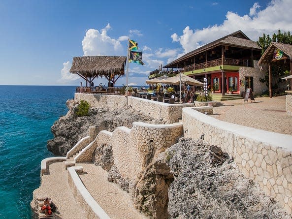 A busy café on a cliff overlooking blue waters.