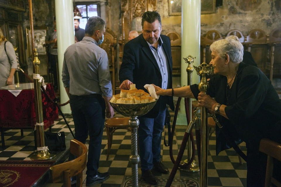 ADDS THAT THEY ARE TAKING BLESSED BREAD AFTER HOLY COMMUNION - In this Sunday, May 24, 2020, photo, a man and an elderly woman take a piece of bread that has been blessed, after receiving Holy Communion in a Greek Orthodox church in the northern city of Thessaloniki, Greece. Priests at the church use a traditional spoon to distribute Holy Communion. Contrary to science, the Greek Orthodox Church says it is impossible for any disease, including the coronavirus, to be transmitted through Holy Communion. (AP Photo/Giannis Papanikos)