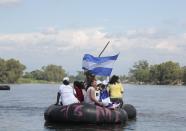 Women from "Caravana de Madres Centroamericanas" (Caravan of Central American Mothers) displays photos of missing migrants and a Salvadorian flag as they ride a raft to cross to Guatemala from the Suchiate river in the border of Ciudad Hidalgo, Chiapas, south of Mexico, December 18, 2013. According to the organizers, the group which is made up of relatives of people who went missing while making their way to the U.S. went to Mexico in the last two weeks to demand that the governments of Mexico and Central America stop the kidnappings and crimes committed by organised criminal groups against migrants. REUTERS/Jorge Dan Lopez (MEXICO - Tags: POLITICS CRIME LAW SOCIETY IMMIGRATION TPX IMAGES OF THE DAY)