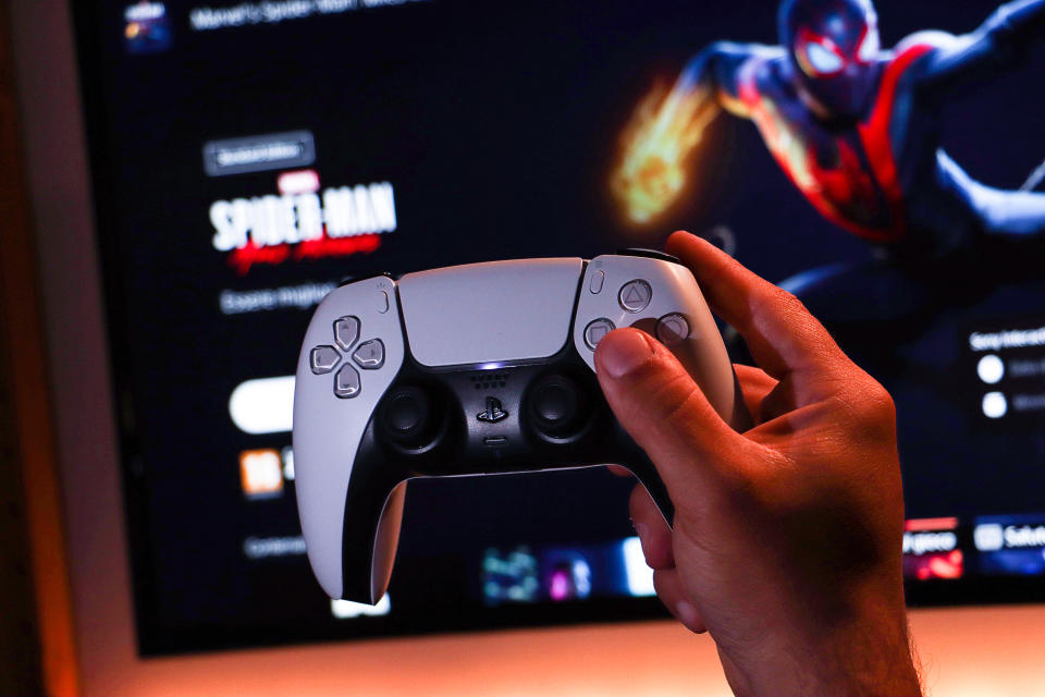 Ancona, Italy - May 16, 2021: Sony Playstation 5 DualSense Controller with Player Hand. In the background you can see the Playstation Plus Store screen with the Marvel&#39;s Spider-Man Miles Morales Standard Edition video game.