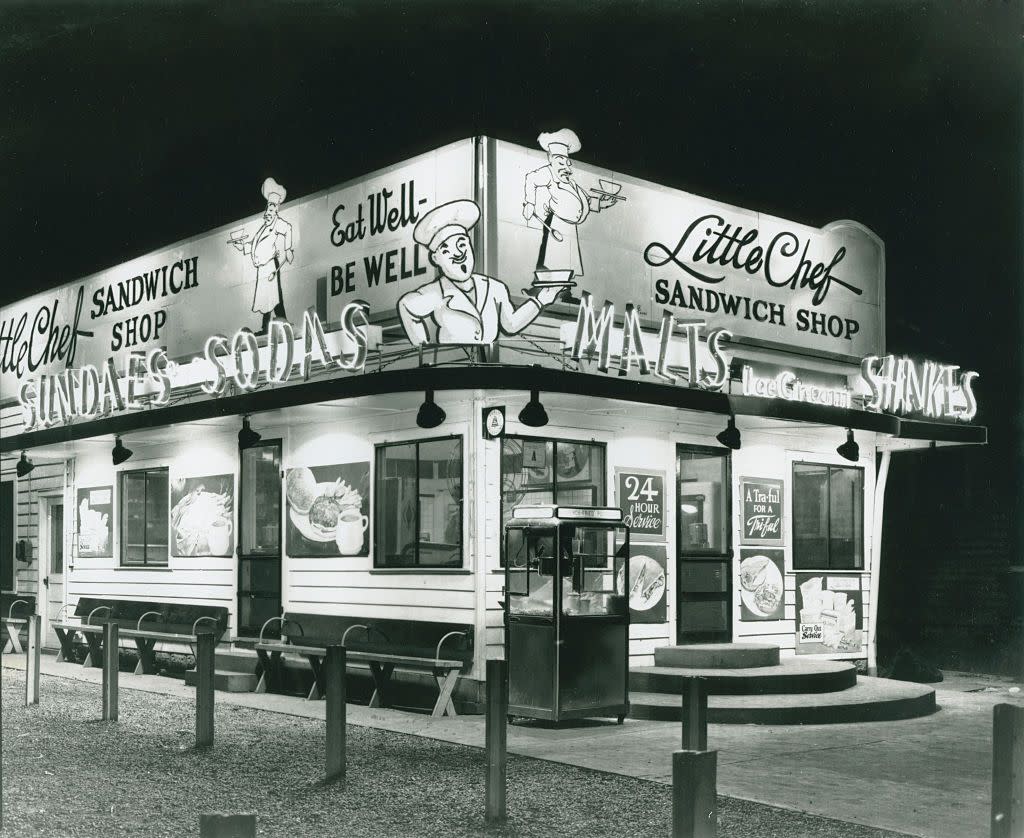 Black and white photograph of Little Chef Sandwich Shop exterior at night with neon signs illuminated.