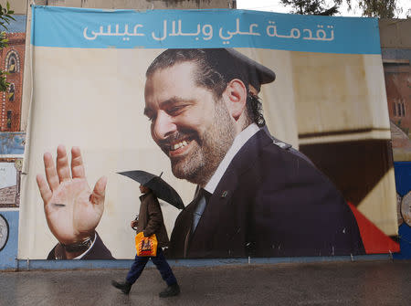 A man holding an umbrella walks past a banner of Lebanese Prime Minister Saad al-Hariri in Beirut, Lebanon February 1, 2019. REUTERS/Mohamed Azakir