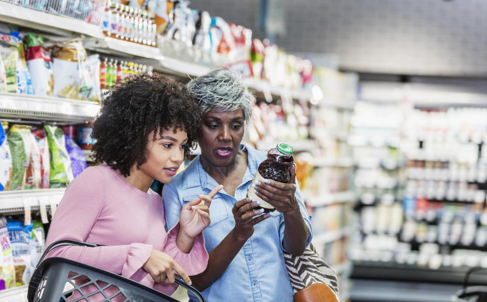 Two women reading the label on a bottle of juice in a grocery store.