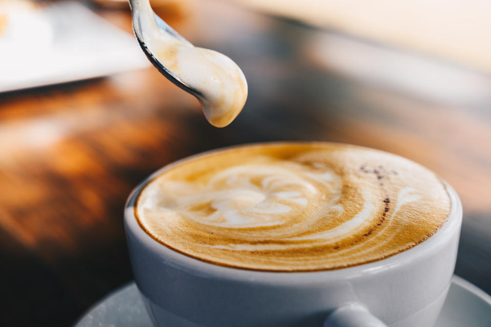 person scooping foam out of a hot latte with a spoon