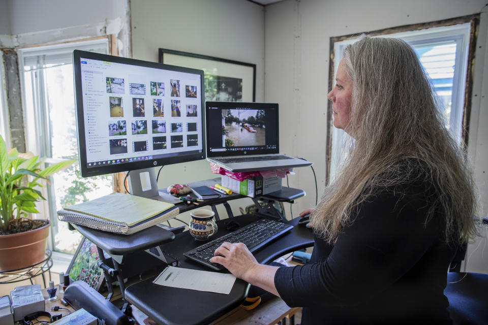 Lisa Edson Neveu, 52, goes through the pictures of 2023 flood while working at the main room of her house in Montpelier, Vt., July 3, 2024 that was damaged by the 2023 flood. A year after catastrophic flooding inundated parts of Vermont, some homeowners are still in the throes of recovery. (AP Photo/ Dmitry Belyakov)