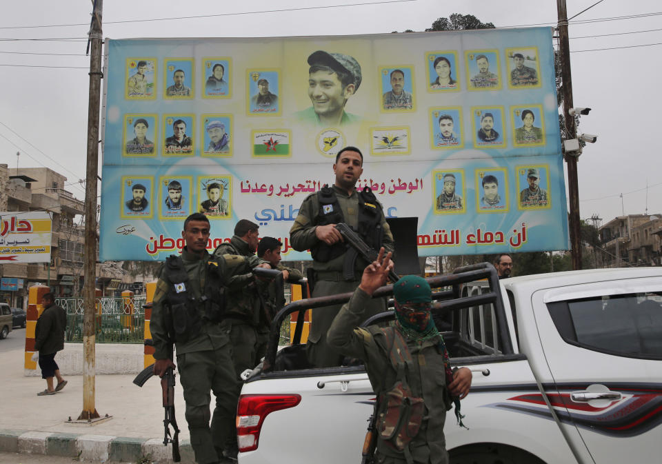 FILE -- In this photo taken on Wednesday, March 28, 2018, members of the Kurdish internal security forces stand on their vehicle in front of a giant poster showing portraits of fighters killed fighting against the Islamic State group, in Manbij, north Syria. The planned U.S. troop withdrawal opens a void in the north and east of Syria, and the conflicts and rivalries among all the powers in the Middle East are converging to fill it. (AP Photo/Hussein Malla, File)