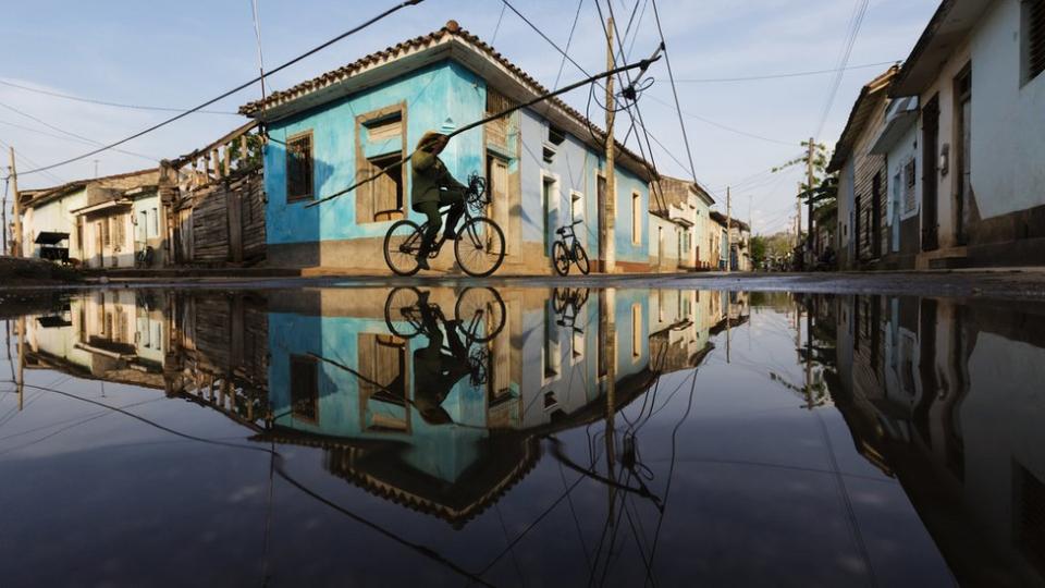 Un hombre camina en bicicleta en una calle inundada de agua en una población de Cuba.