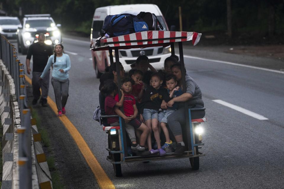 Migrants, many of them children, ride on a motorized bike taxi as other migrants walk along the Huehuetan highway in Chiapas state, Mexico, early Tuesday, June 7, 2022. The group left Tapachula on Monday, tired of waiting to normalize their status in a region with little work and still far from their ultimate goal of reaching the United States. (AP Photo/Marco Ugarte)